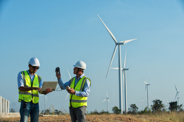 two Asian male engineers working on site with wind turbine propeller and clear blue sky on the background. Alternative energy, environmental friendly for the future. clean energy innovation.