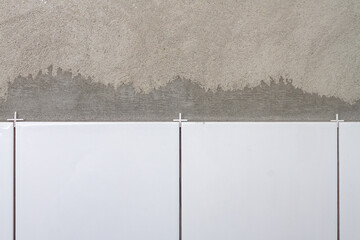 White ceramic tiles laid on a concrete gray wall in the bathroom, new tiles, the process of laying tiles on the wall