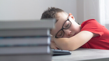 Fototapeta na wymiar A teenage Caucasian schoolboy with glasses is tired of lessons, school, homework and sleeps at his desk