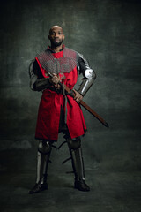 Medieval knight. Portrait of brutal african man, medieval warrior wearing armour isolated over dark...
