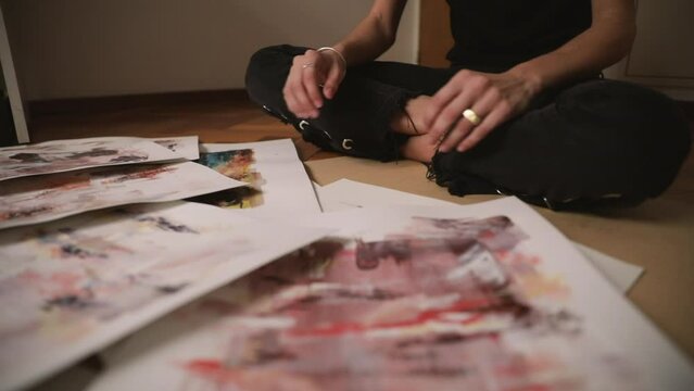 Young female artist arranging her paintings in the art studio.Colorful paintings and drawings with beautiful colors and brushwork texture and pattern.