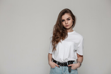 Pretty serious woman in white mockup t-shirt stands in studio on a gray background