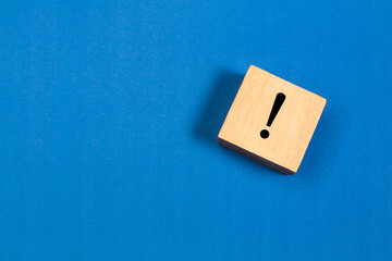 Cubo de juguete de madera con un signo de exclamación sobre un fondo azul liso y aislado. Vista superior y de cerca. Copy space