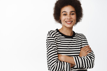 Fototapeta premium Portrait of beautiful millennial african girl with afro hair, casual clothes, cross arms over chest and smiling happy at camera