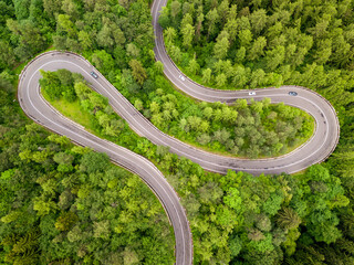 Winding road trough dense forest. Aerial drone view, top down