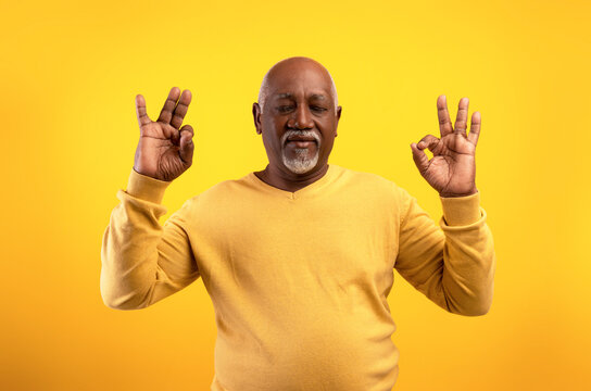 Stress relief concept. Edlerly African American man meditating with closed eyes, keeping calm on orange background