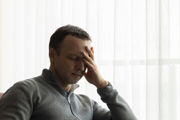 Tired man with closed eyes sitting near a window