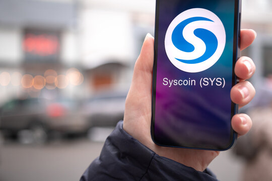 Syscoin coin symbol. Trade with cryptocurrency, digital and virtual money, mobile banking. Hand with smartphone, screen with crypto icon close-up photo