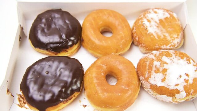 Closeup macro of collection assorted donuts in box with two people hands placing boston cream and powder sugar dessert doughnut for delivery 