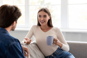 Cheerful young european husband and woman with cups of hot drink talk and spending weekend together