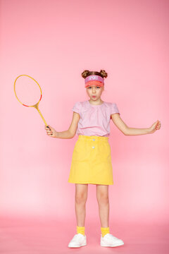 Photo of a girl with a happy positive smile, a sports tennis racket playing a game, isolated on a pink background