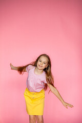 A funny little blonde girl of 10 years old in everyday bright clothes poses alone on a pink studio...