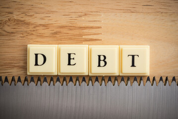 Word DEBT on saw blade with wooden table background macro shot. Personal loan financial, risk management, debt business or investment concept.