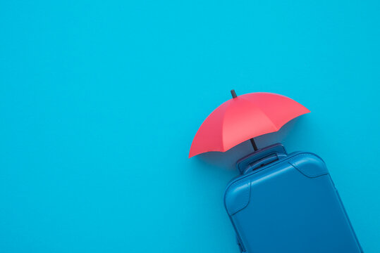 Travel insurance business concept. Red umbrella cover suitcases travelers on blue background copy space. Travel insurance covers loss suitcase, flight delays, cancellations, accident, medical expenses