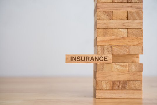 Life, health, property or credit insurance business concept. Insurance is risk control management plan. Wooden block tower stacking game with word INSURANCE on wooden table background with copy space.