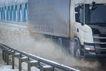 Big water splash from wheels of truck on road with puddles.