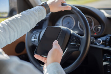 man using mobile smart phone inside a car. Driver hand holding blank black screen smartphone, searching address and pin location via map navigator application, transportation technology