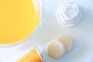 Fototapeta premium Vitamin C dissolvable tablets out of a tube on a white table, vitamin C drink in foreground, selective focus