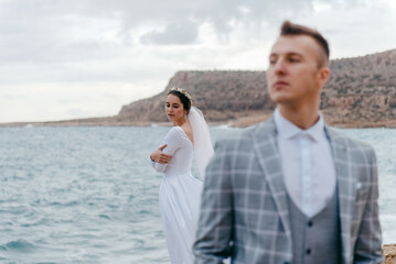 Portrait of happy newlyweds, bride and groom, standing on a rocky shore near the sea. A wonderful young couple