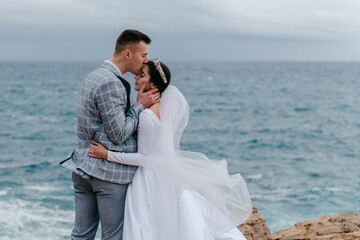 The newlyweds gently hug on the rocks by the sea and enjoy the nature of Cyprus