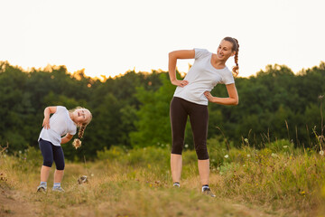 mom and daughter doing exercise in nature near the forest