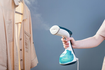 female hand with steamer and shirt on blue background - obrazy, fototapety, plakaty