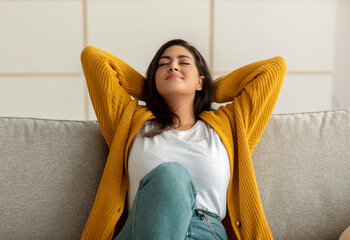 Life is good. Young arab lady leaning back on sofa with closed eyes and hands behind head, resting...