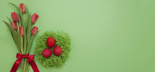 Easter Spring Holiday celebration. Egg nest and fresh red tulip on green background, overhead