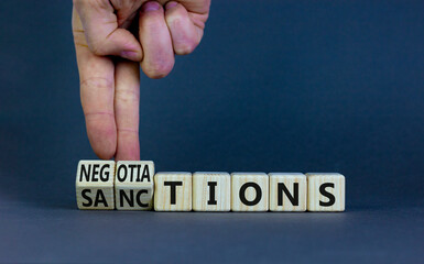 Sanctions or negotiations symbol. Businessman turns cubes, changes the word sanctions to negotiations. Beautiful grey table, grey background, copy space. Business, sanction or negotiation concept.