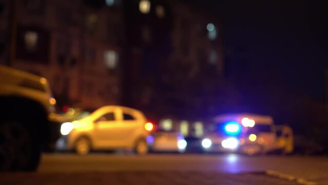 The emergency lights of a police car are out of focus at night on the side of the road with other cars. Late night traffic lights in the city.