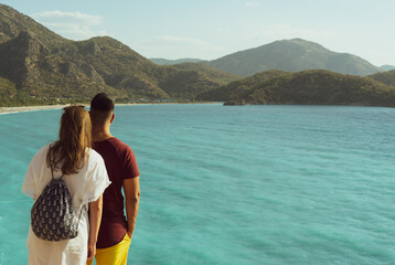 A couple in love (view from the back) stand nearby and look at the sea and the landscape