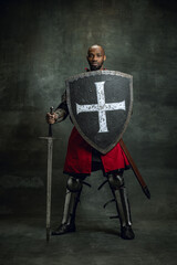Portrait of medieval warrior, dark skinned bald knight with dirty wounded face holding shield and...