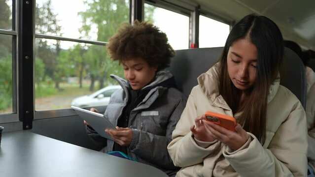 Addicted to gadgets mixed race schoolboy and asian schoolgirl ignoring each other and using tablet and cellphone while riding school bus after studies. Online communication, phubbing concept