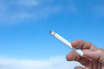 青空と煙草を男性の持つ手