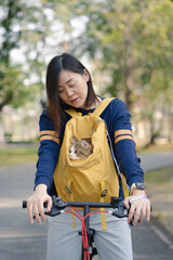 asian woman biking bicycle with her cat in backpack at park