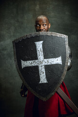 Portrait of medieval warrior, dark skinned bald knight with dirty wounded face holding shield and...