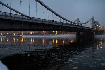 The beautiful view on the bridge in the night and golden reflection in the river with ice