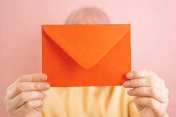 Woman hands holding red romantic envelope and looking at camera isolated on a pink background. Celebrating International Women Day, 8 march, mothers day, birthday.