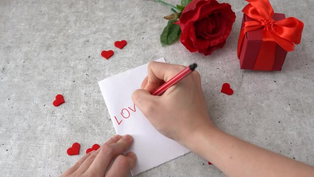 Woman writes massage Love You for 14 February celebration. Hearts, rose and red gift box on the table