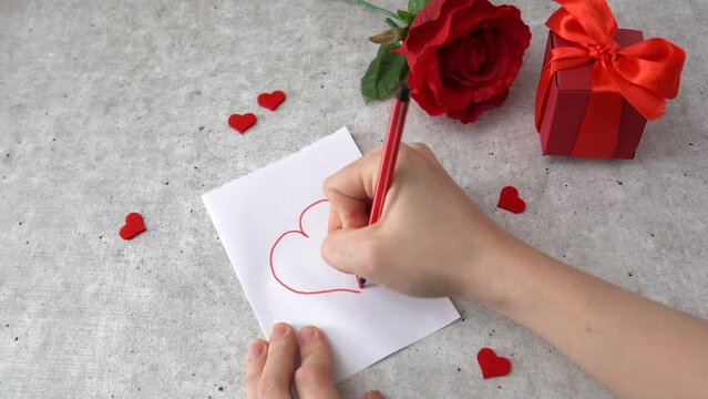 Woman draws a heart for 14 February celebration. Hearts, rose and red gift box on the table