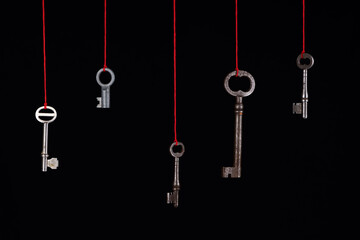Fototapeta na wymiar A lot of different old keys from different locks, hanging from the top on red strings. Finding the right key, encryption, concept. Retro vintage keys on a dark background..