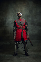 Dreams. Vintage style portrait of stylish dark skinned man, medieval warrior or knight in sunglasses and headphones isolated over dark background. Comparison of eras, history