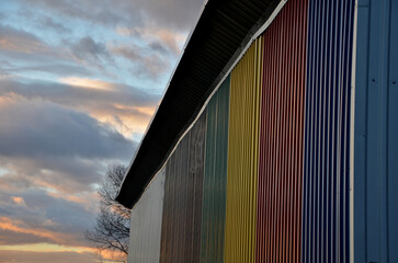 sheet metal wall of an industrial hall made of corrugated sheet metal in bright colors. Striped sheets complement the interestingly colored sky of the evening sky