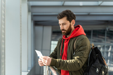 Waist up portrait of the young caucasian man standing at the airport lounge and checking his...
