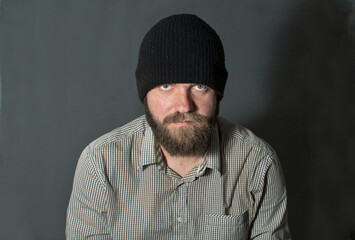 Fototapeta premium a young man with a beard in a knitted hat looks at the portrait from under his brows.