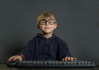 a boy with glasses is sitting at a computer, he stares intently at the monitor