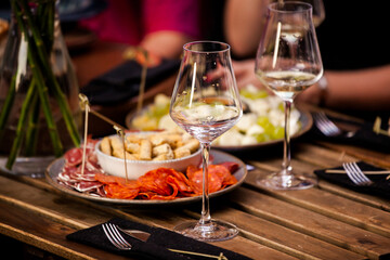 Glasses of wine and plate with fruits and cheese placed on wooden table near chairs on sunny summer day on terrace