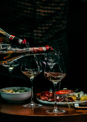 Glasses of wine and plate with fruits and cheese placed on wooden table near chairs on sunny summer day on terrace