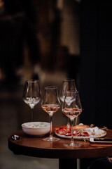Glasses of wine and plate with fruits and cheese placed on wooden table near chairs on sunny summer day on terrace