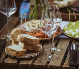 Glasses of wine and plate with fruits and cheese placed on wooden table near chairs on sunny summer day on terrace